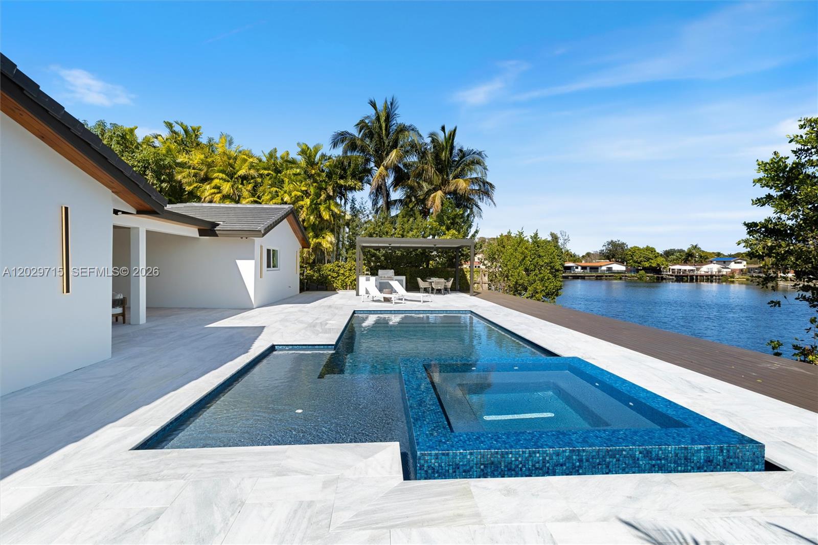 A modern house features a tiled patio, a swimming pool with a spa, and waterfront views — 19721 NE 23rd Ave # 19721, Miami FL 33180, MIAMI, FL