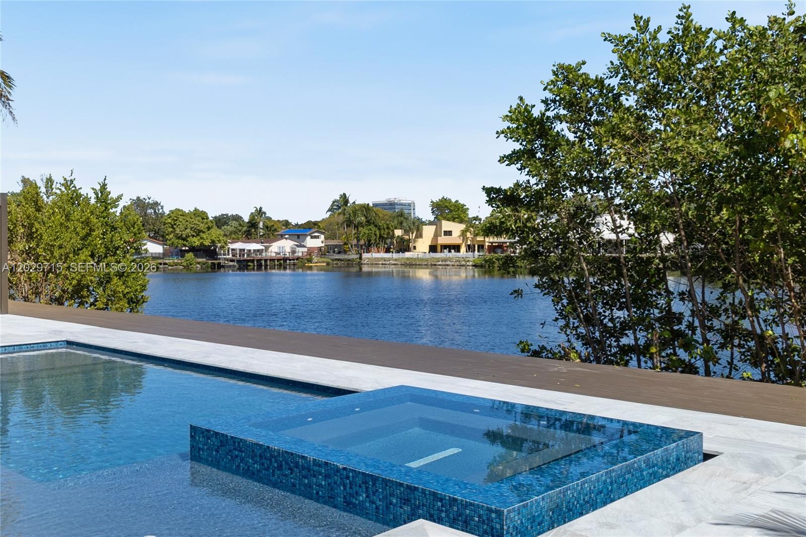 A tiled infinity-edge spa overlooks a swimming pool and a lake with distant houses — 19721 NE 23rd Ave # 19721, Miami FL 33180, MIAMI, FL