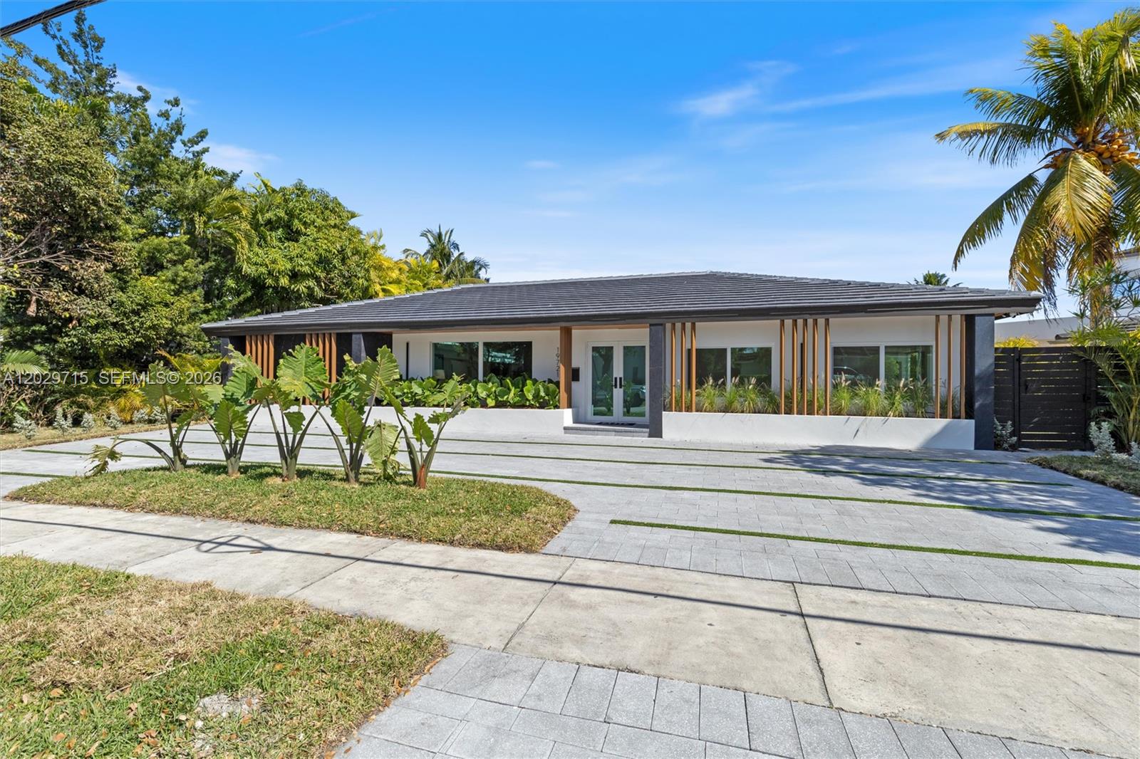 A modern single-story house features a paved driveway, vertical wood accents, and lush landscaping — 19721 NE 23rd Ave # 19721, Miami FL 33180, MIAMI, FL