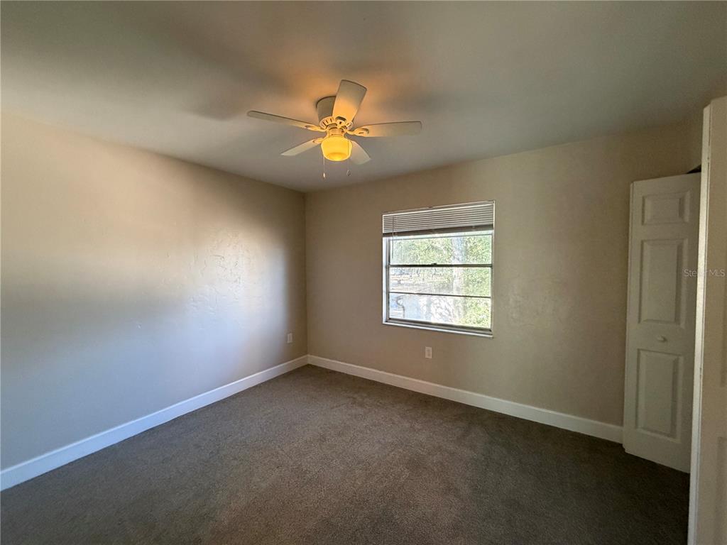 An empty bedroom features beige walls, brown carpeting, a ceiling fan, and a window — 1718 SW 69TH TERRACE UNIT A, GAINESVILLE, FL