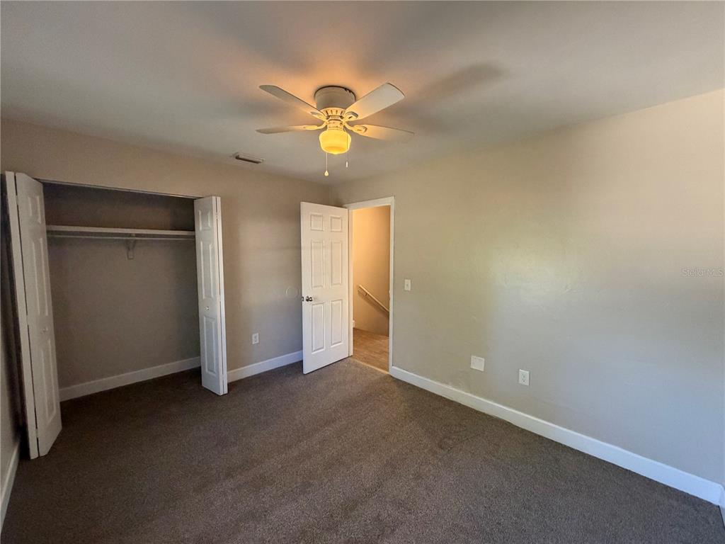 A bedroom features gray carpet, beige walls, a ceiling fan, and an open closet — 1718 SW 69TH TERRACE UNIT A, GAINESVILLE, FL
