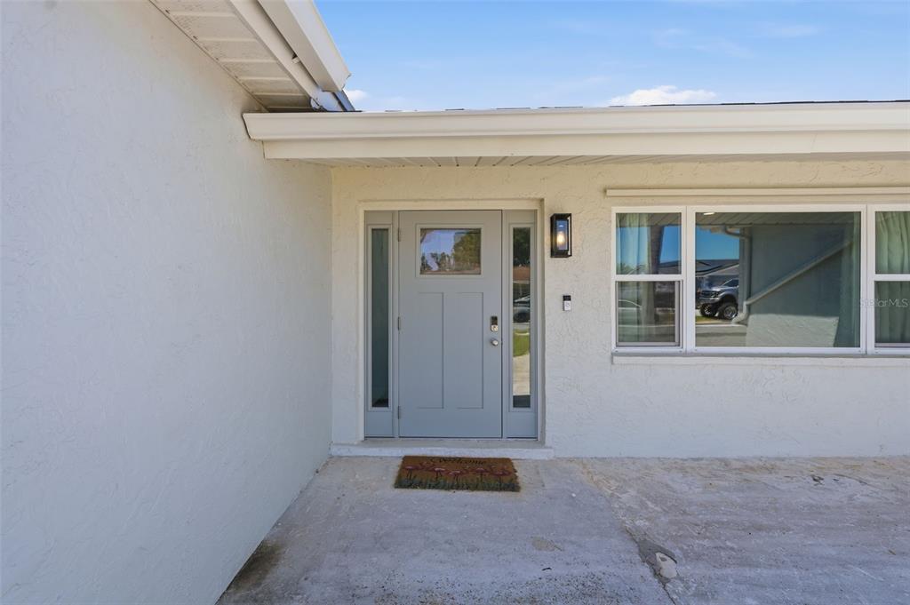 A light gray front door with sidelights is centered on a white stucco exterior wall — 9276 N 79TH AVENUE, SEMINOLE, FL