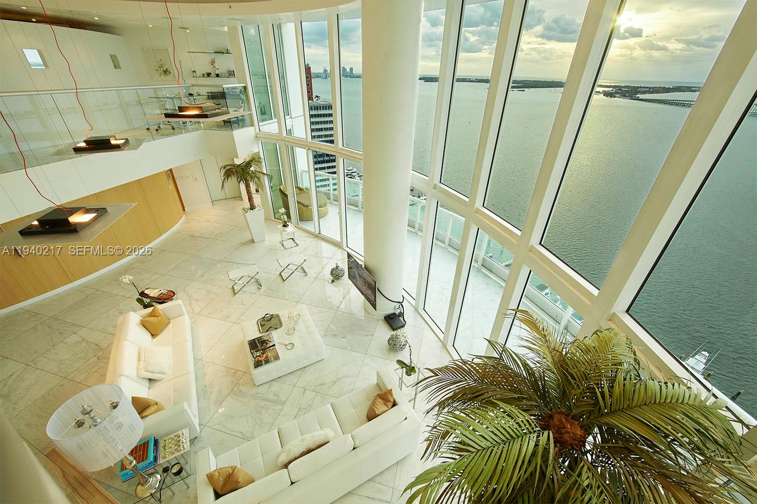 A high-ceilinged living room features white marble floors, modern furniture, and floor-to-ceiling windows overlooking water — 1643 Brickell Ave # 2902, Miami FL 33129, MIAMI, FL
