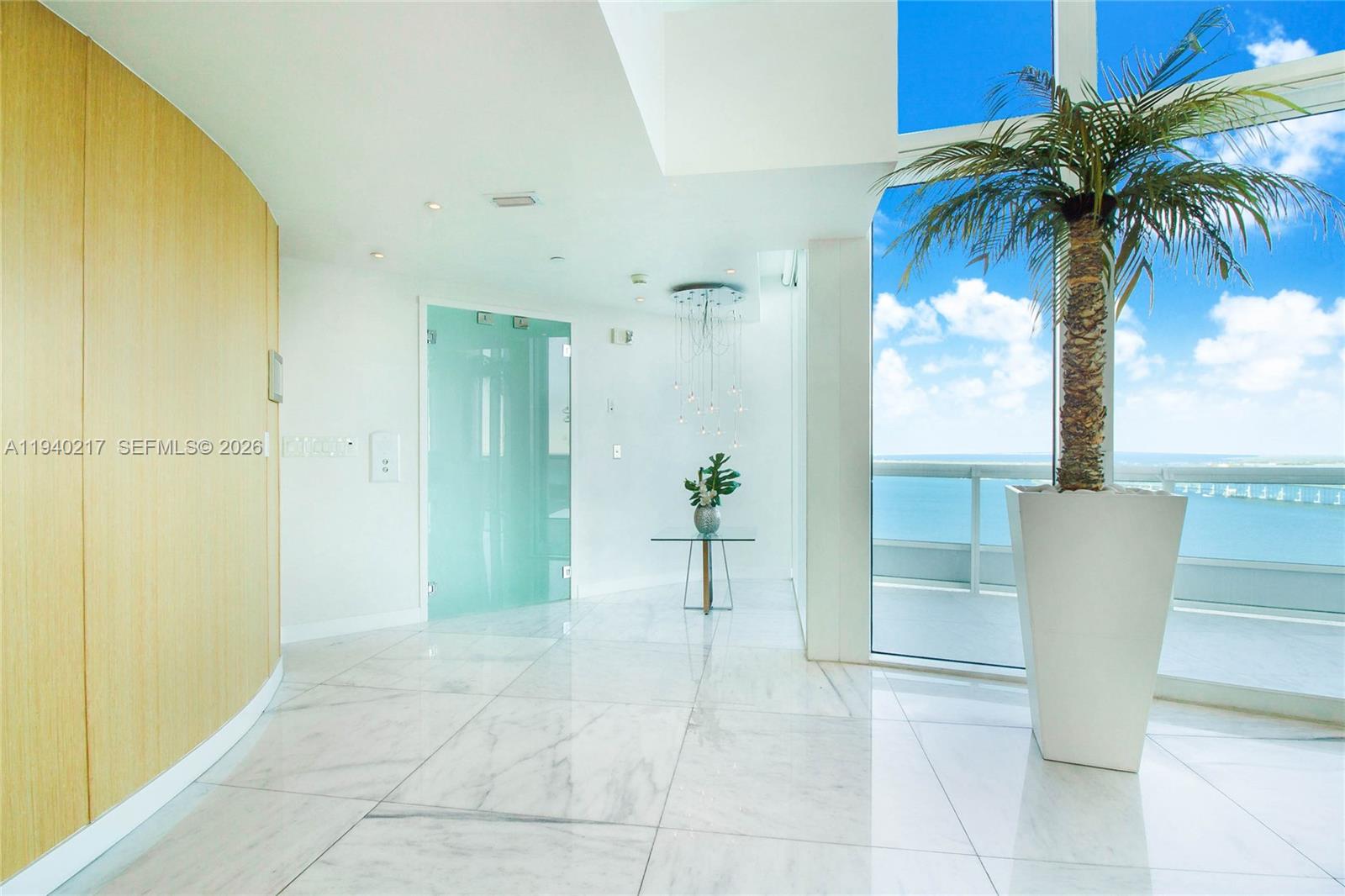 A bright, modern foyer features marble floors, a glass door, and a large potted palm — 1643 Brickell Ave # 2902, Miami FL 33129, MIAMI, FL