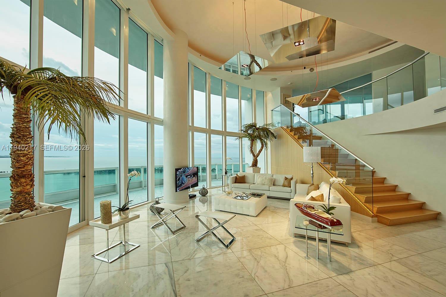 A bright, double-height living room features marble floors, floor-to-ceiling windows, and a wooden staircase — 1643 Brickell Ave # 2902, Miami FL 33129, MIAMI, FL