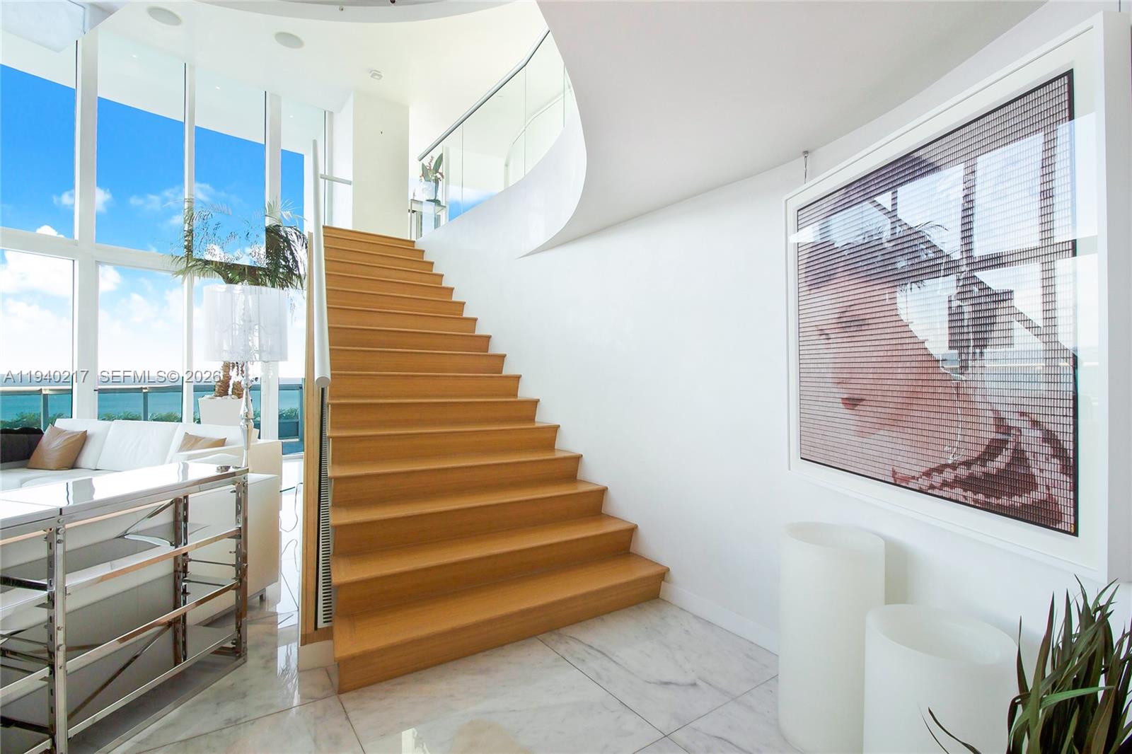 A modern interior features a wooden staircase, marble flooring, and a large portrait on the wall — 1643 Brickell Ave # 2902, Miami FL 33129, MIAMI, FL