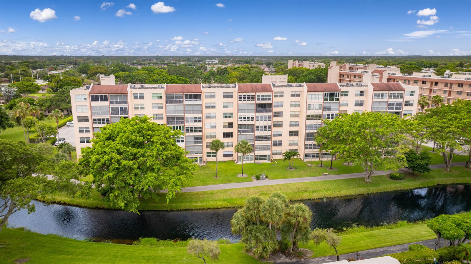 An aerial view of a multi-story apartment building situated beside a canal and green lawn — 14527 Bonaire Boulevard # 203, Delray Beach FL 33446, DELRAY BEACH, FL