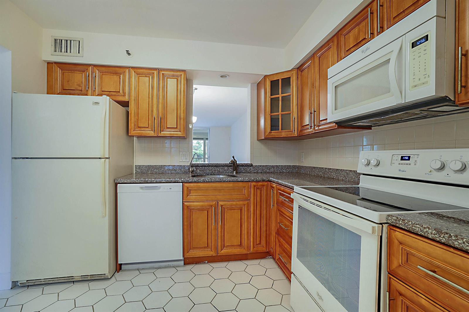 A kitchen with wood cabinets, white appliances, granite countertops, and white hexagonal floor tiles — 14527 Bonaire Boulevard # 203, Delray Beach FL 33446, DELRAY BEACH, FL
