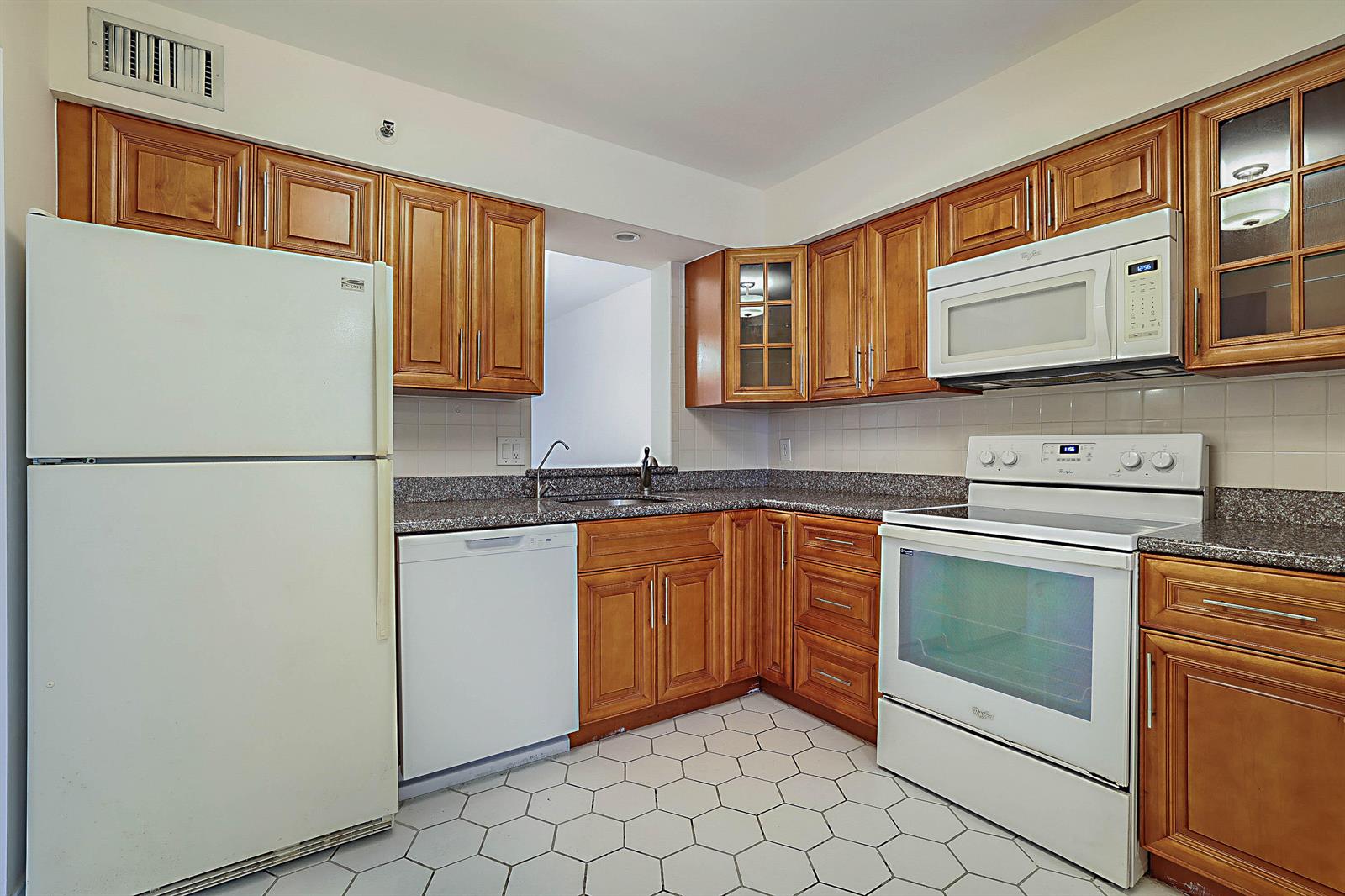 A kitchen with wood cabinets, white appliances, granite countertops, and white hexagonal floor tiles — 14527 Bonaire Boulevard # 203, Delray Beach FL 33446, DELRAY BEACH, FL