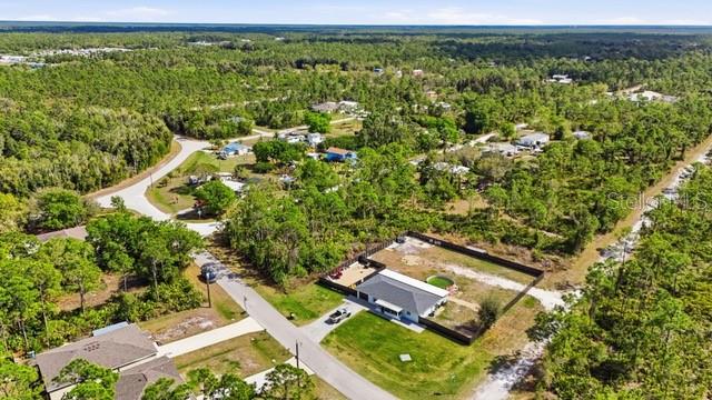 An aerial view shows a house with a fenced yard surrounded by dense forest — 12143 CARTOUCHE AVENUE, PUNTA GORDA, FL