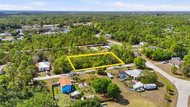 An aerial view shows a vacant, rectangular lot outlined in yellow amidst a wooded neighborhood — 12143 CARTOUCHE AVENUE, PUNTA GORDA, FL