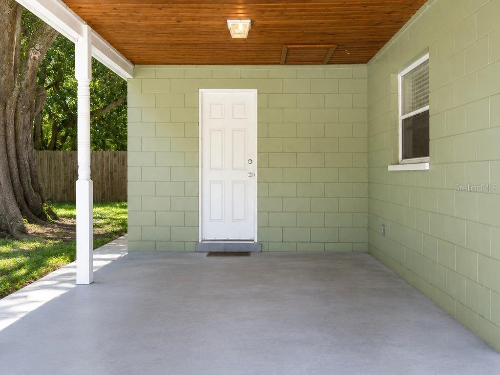 A covered concrete patio features light green block walls, a wood ceiling, and a white door — 516 TANGLEWOOD DRIVE, AUBURNDALE, FL