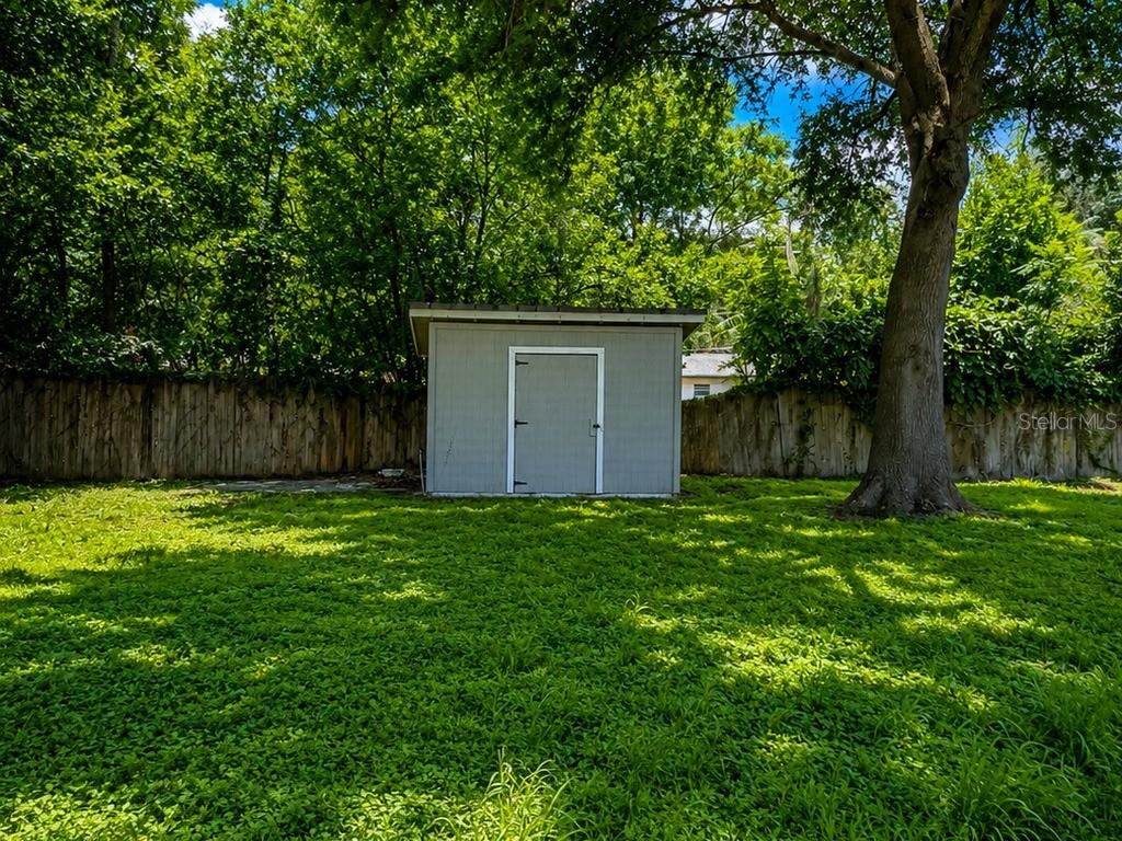 A gray storage shed sits in a grassy backyard in front of a wooden fence — 516 TANGLEWOOD DRIVE, AUBURNDALE, FL