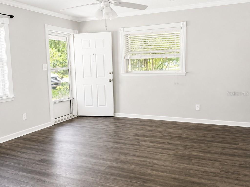 A living room with light gray walls, dark wood-look flooring, a ceiling fan, and windows — 516 TANGLEWOOD DRIVE, AUBURNDALE, FL