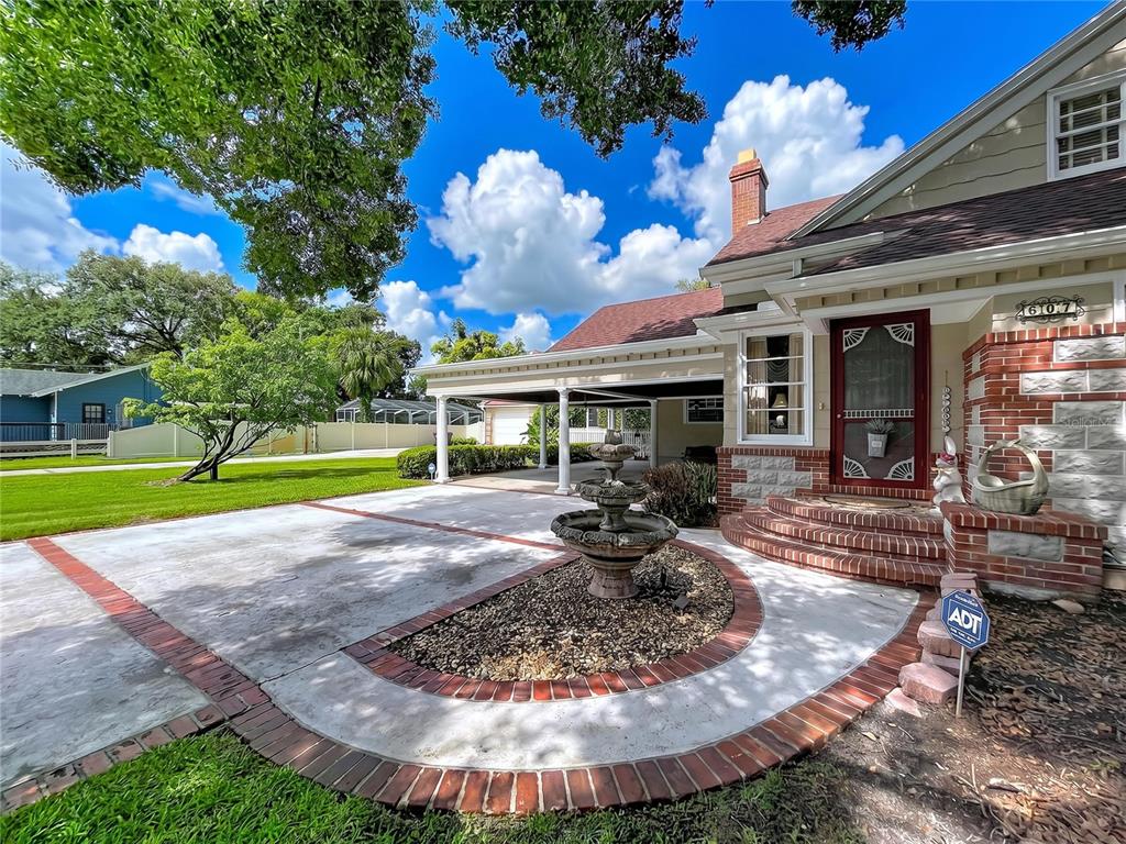 A house exterior features a brick-trimmed concrete driveway, a tiered fountain, and a covered carport — 607 N MERRIN STREET, PLANT CITY, FL