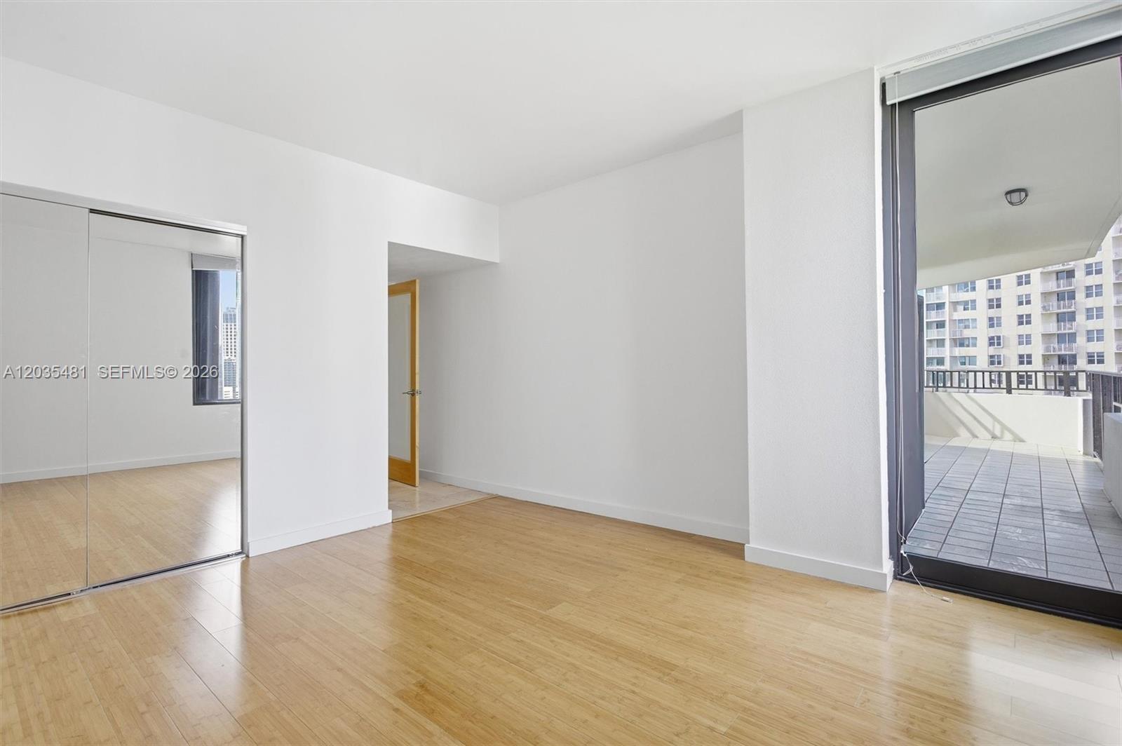 An empty room features light wood flooring, mirrored closet doors, and a balcony with city views — 520 SE Brickell Key Dr # A1615, Miami FL 33131, MIAMI, FL