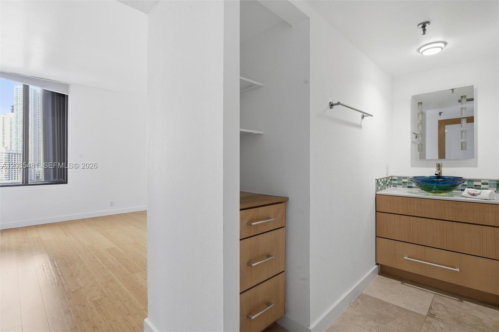 A bathroom with a wood vanity and blue glass sink sits beside a bedroom area — 520 SE Brickell Key Dr # A1615, Miami FL 33131, MIAMI, FL