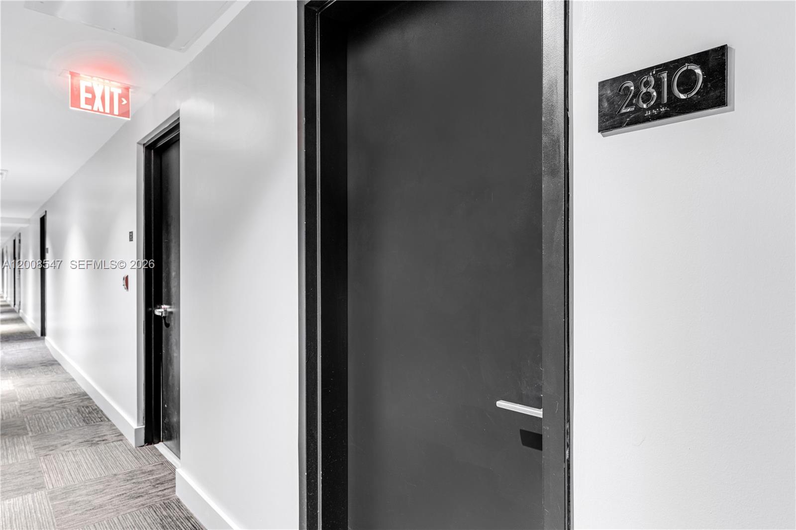 A hallway features a dark door labeled 2810 and an illuminated red exit sign — 121 NE 34th St # 2810, Miami FL 33137, MIAMI, FL