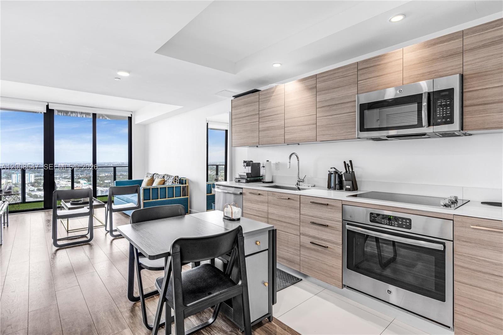 A modern kitchen with wood-grain cabinets and stainless steel appliances opens to a living area — 121 NE 34th St # 2810, Miami FL 33137, MIAMI, FL