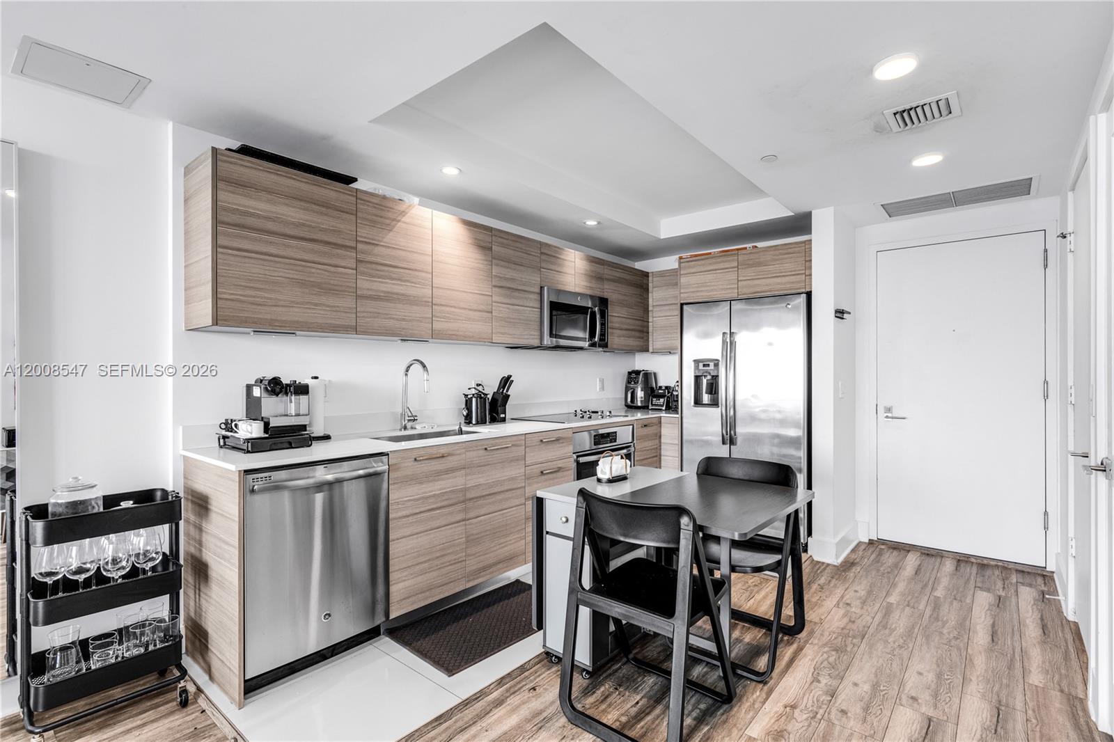 A modern kitchen features wood-grain cabinets, stainless steel appliances, and a small dining table — 121 NE 34th St # 2810, Miami FL 33137, MIAMI, FL