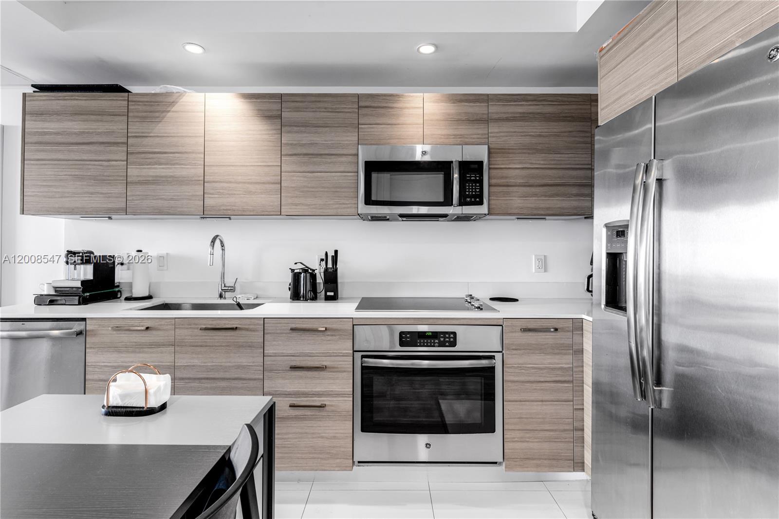 A modern kitchen features wood-grain cabinets, stainless steel appliances, and white countertops — 121 NE 34th St # 2810, Miami FL 33137, MIAMI, FL