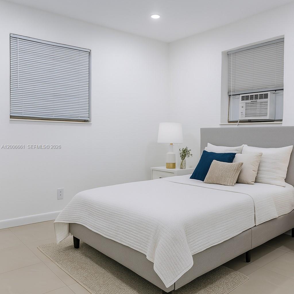 A bedroom features a gray upholstered bed, white walls, tile flooring, and two windows — 1046 Foster Rd # 0, Hallandale Beach FL 33009, HALLANDALE BEACH, FL