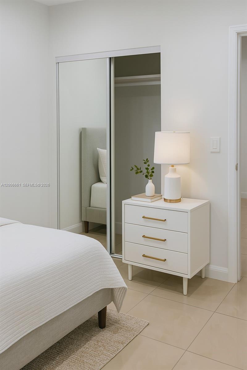 A bedroom features a white nightstand with gold handles, a table lamp, and mirrored closet doors — 1046 Foster Rd # 0, Hallandale Beach FL 33009, HALLANDALE BEACH, FL