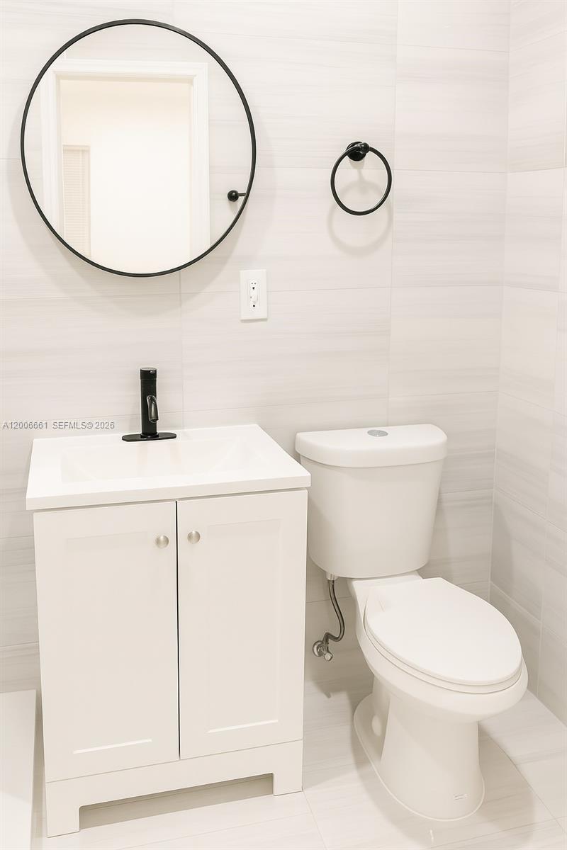 A modern bathroom features a white vanity, a round black mirror, and a white toilet — 1046 Foster Rd # 0, Hallandale Beach FL 33009, HALLANDALE BEACH, FL