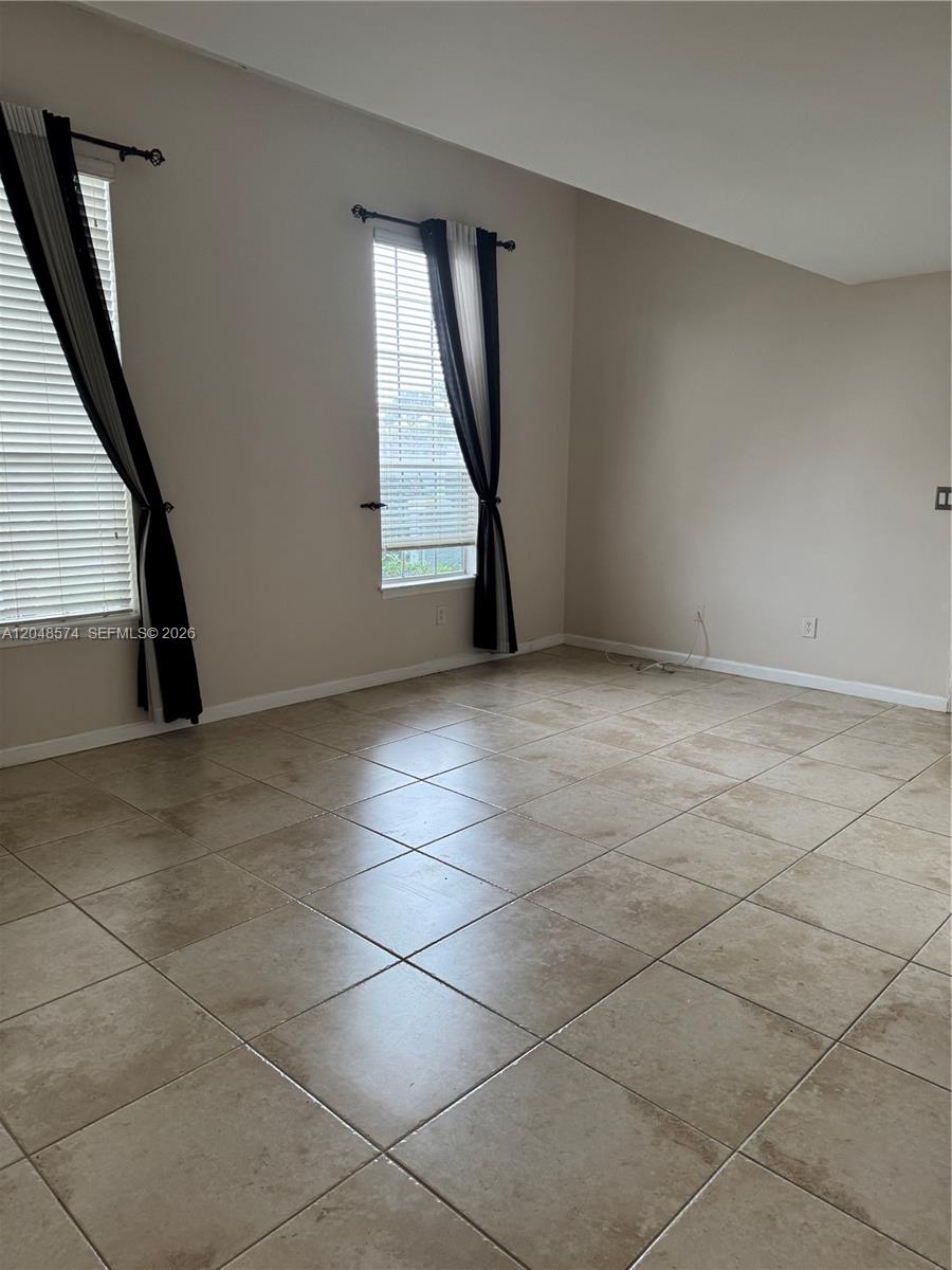 An empty room features beige walls, tiled flooring, and two windows with black curtains — 1205 Crystal Way, Delray Beach FL 33444, DELRAY BEACH, FL