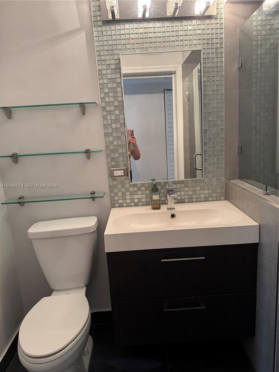 A bathroom features a dark wood vanity, glass shelving, and a mosaic tile backsplash — 1205 Crystal Way, Delray Beach FL 33444, DELRAY BEACH, FL
