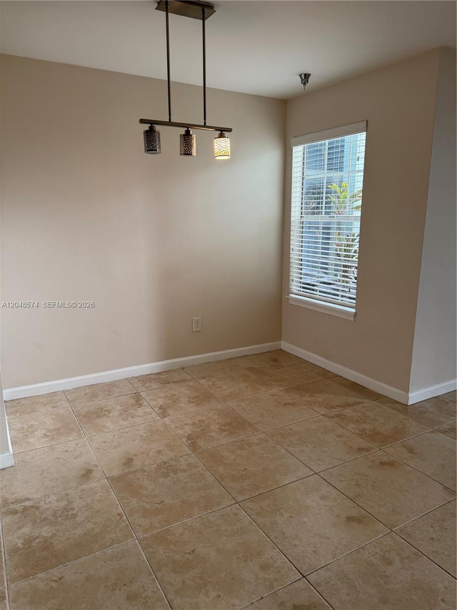 This dining area features tan tile flooring, beige walls, and a modern three-light pendant fixture — 1205 Crystal Way, Delray Beach FL 33444, DELRAY BEACH, FL