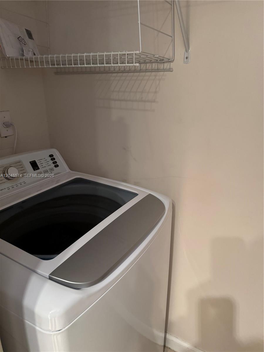 A white top-loading washing machine sits in a closet with a wire shelf above — 1205 Crystal Way, Delray Beach FL 33444, DELRAY BEACH, FL