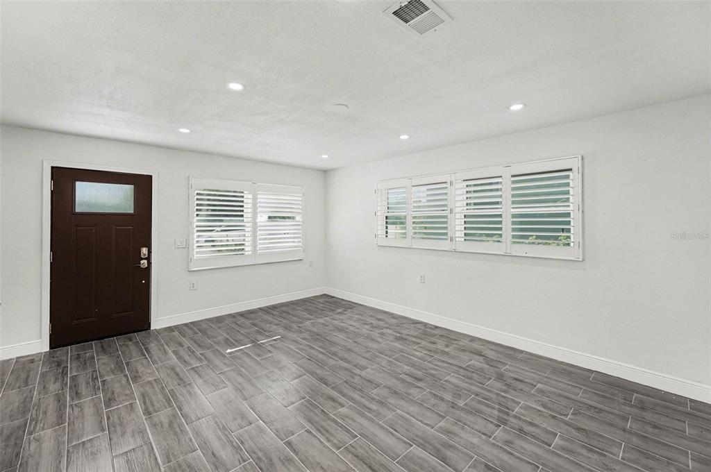 An empty room features white walls, gray wood-look tile flooring, recessed lighting, and plantation shutters — 318 BATH STREET, TARPON SPRINGS, FL