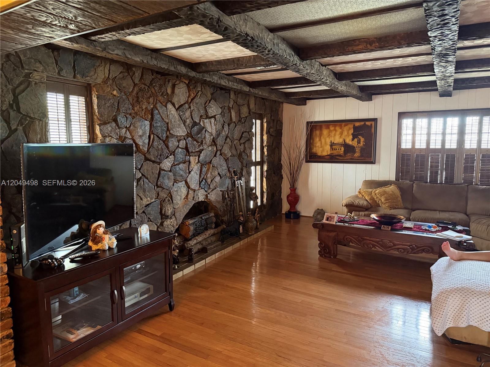 A living room features a stone fireplace, wood-beamed ceiling, and hardwood flooring — 291 W 59th St, Hialeah FL 33012, HIALEAH, FL