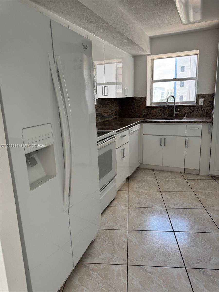 A kitchen features white cabinets, a white refrigerator, a white stove, and brown stone countertops — 6039 COLLINS AV # 537, Miami Beach FL 33140, MIAMI BEACH, FL
