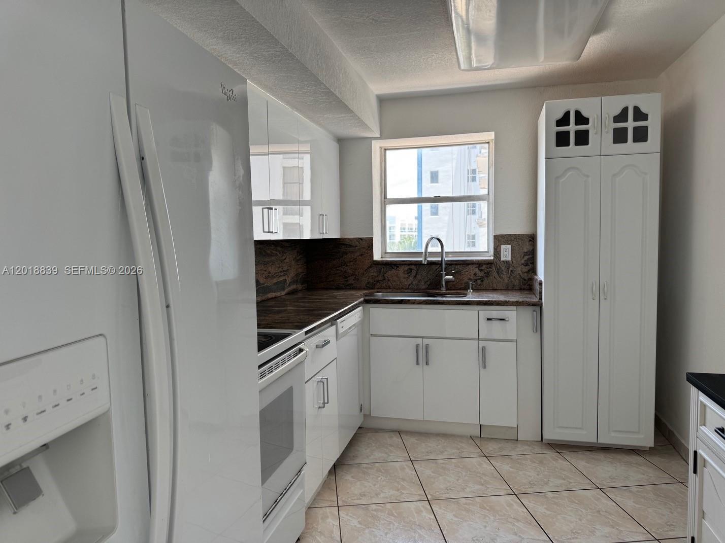 A kitchen features white cabinets, a dark granite countertop, and a window above the sink — 6039 COLLINS AV # 537, Miami Beach FL 33140, MIAMI BEACH, FL