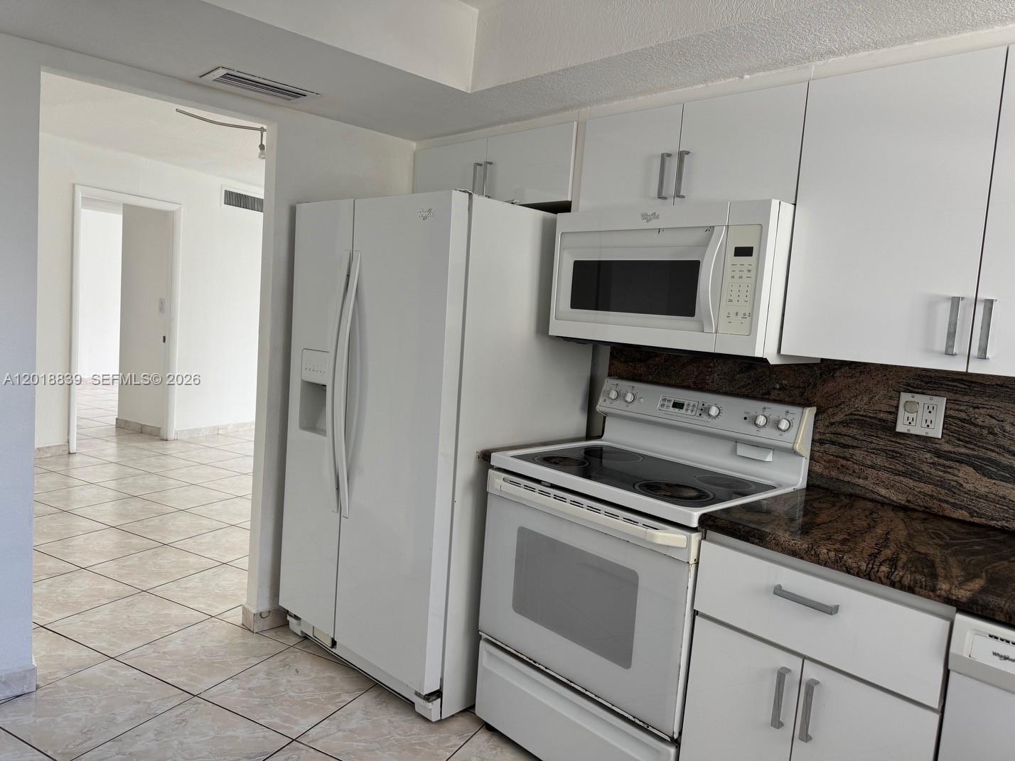 A kitchen features white appliances, white cabinets, and dark granite countertops — 6039 COLLINS AV # 537, Miami Beach FL 33140, MIAMI BEACH, FL