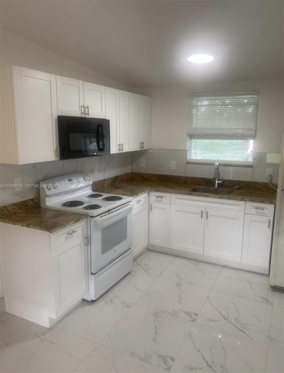 A kitchen features white cabinets, granite countertops, a white stove, and light-colored tile flooring — 6045 Buchanan St # 1, Hollywood FL 33024, HOLLYWOOD, FL