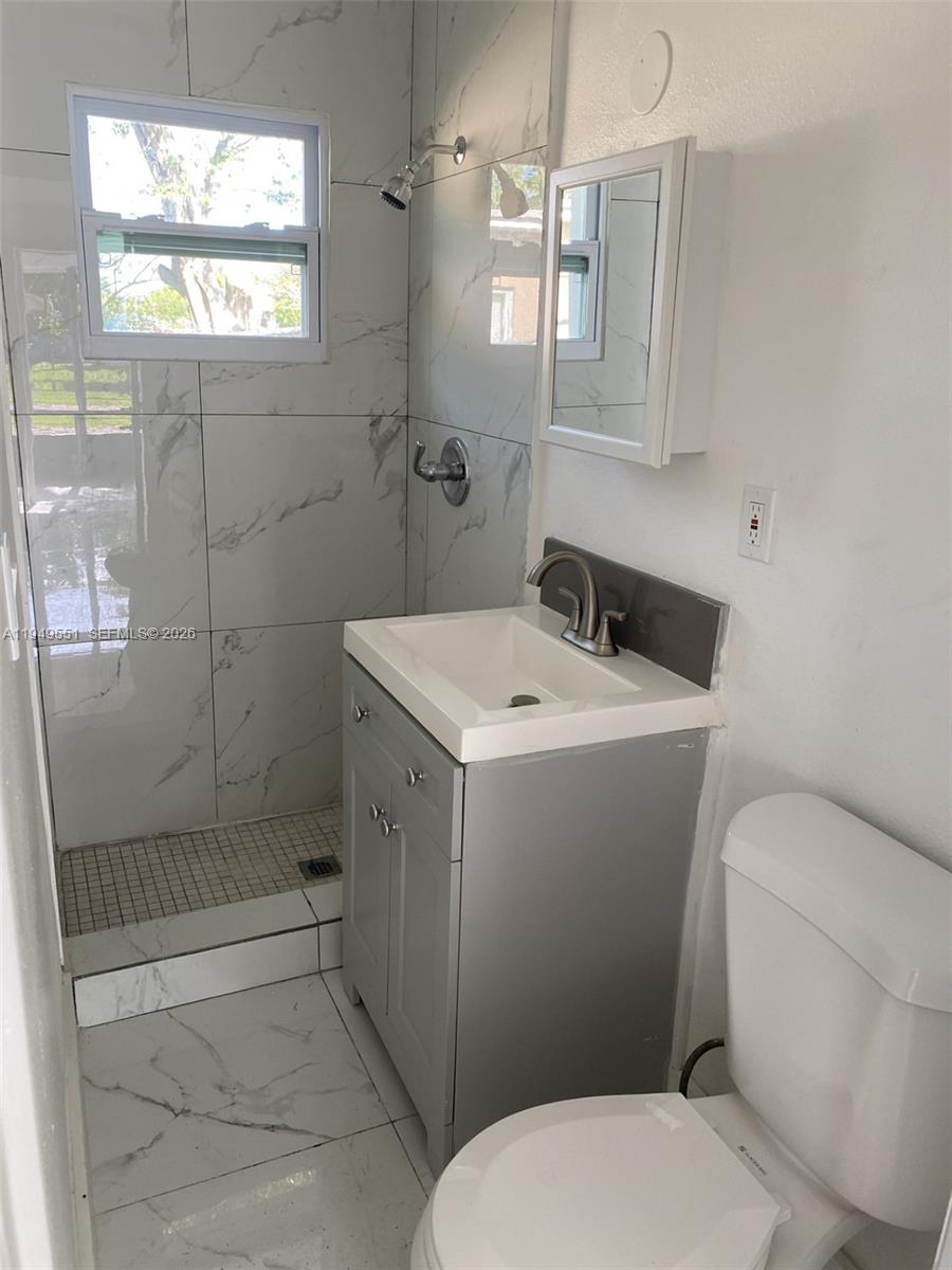 A small bathroom features a gray vanity, a white toilet, and a tiled walk-in shower — 6045 Buchanan St # 1, Hollywood FL 33024, HOLLYWOOD, FL