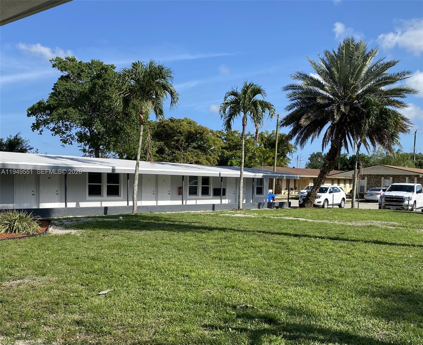 A single-story white building with multiple entrances sits behind a lawn with palm trees — 6045 Buchanan St # 1, Hollywood FL 33024, HOLLYWOOD, FL