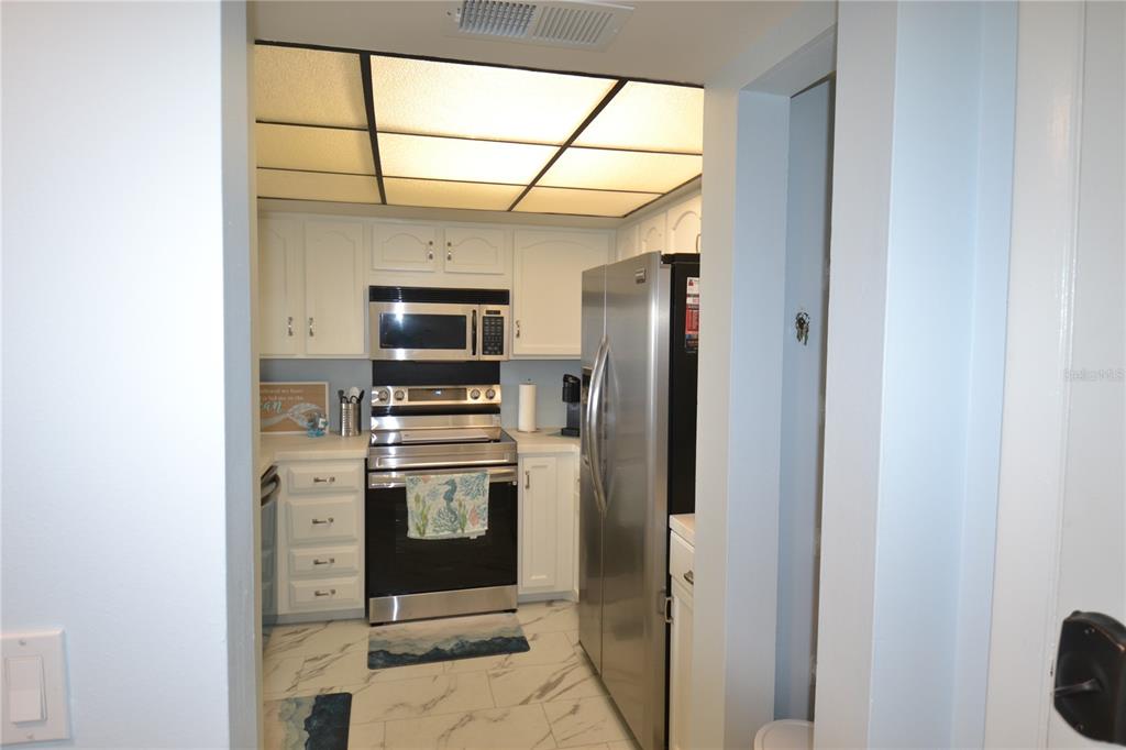 A galley kitchen features white cabinets, stainless steel appliances, and a drop ceiling with lighting — 238 MARINER DRIVE, TARPON SPRINGS, FL