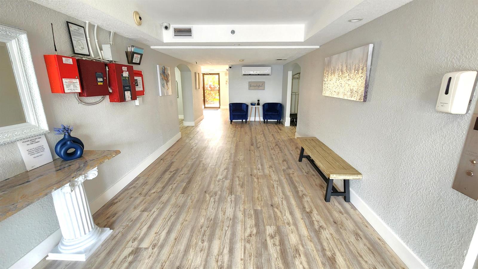 A bright lobby features wood-look flooring, a wooden bench, two blue chairs, and wall art — 2255 Lindell Boulevard # 4111, Delray Beach FL 33444, DELRAY BEACH, FL