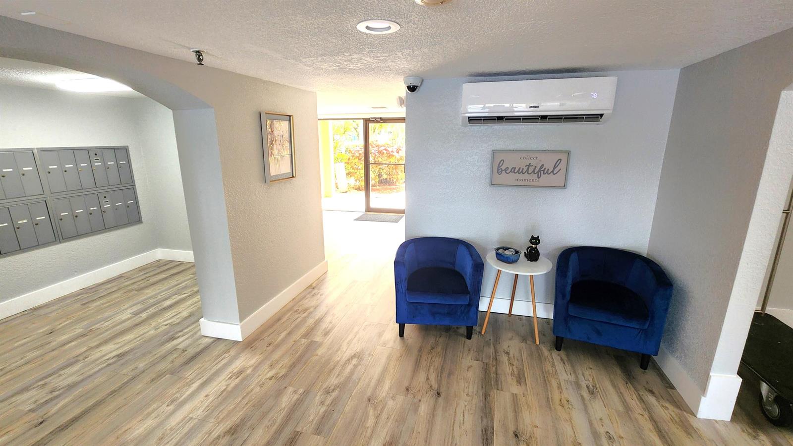 A lobby area features wood-look flooring, two blue velvet chairs, mailboxes, and a wall-mounted AC — 2255 Lindell Boulevard # 4111, Delray Beach FL 33444, DELRAY BEACH, FL