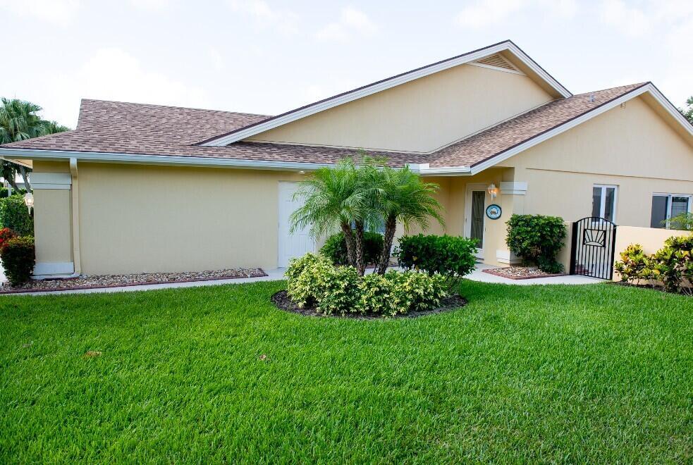 A single-story house with tan stucco walls, a brown shingled roof, and a landscaped front yard — 114 Beach Summit Court, Jupiter FL 33477, JUPITER, FL