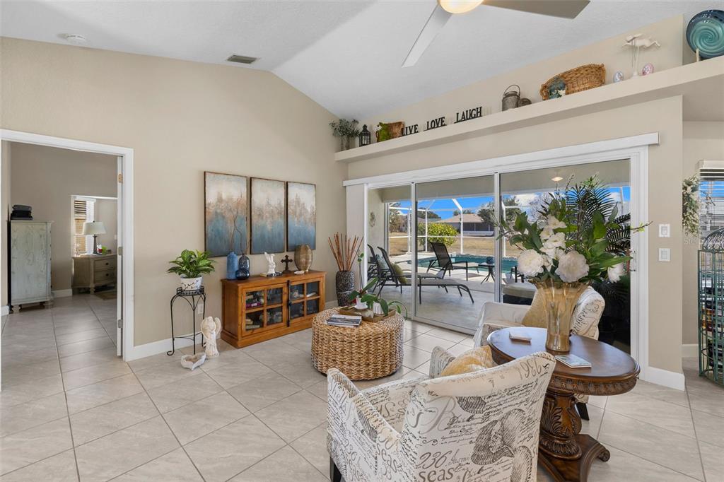 A living room with tile floors, vaulted ceilings, and sliding glass doors opening to a pool — 26549 VALPARAISO DRIVE, PUNTA GORDA, FL