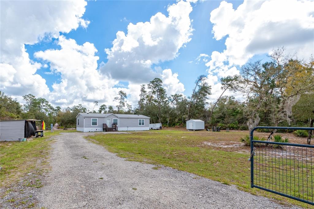 A light gray manufactured home sits on a large, grassy lot with a gravel driveway — 42300 FONSECA LANE, DELAND, FL