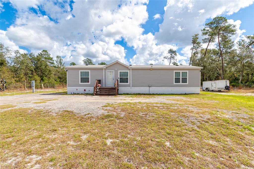 A single-story manufactured home with light gray siding sits on a large gravel lot — 42300 FONSECA LANE, DELAND, FL