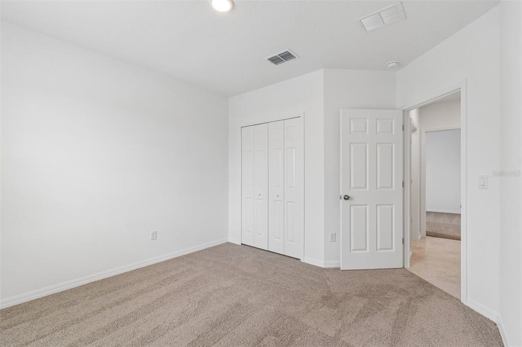 An empty bedroom with white walls, beige carpet, a bi-fold closet, and an open doorway — 8437 FOX DEN COVE, LAKELAND, FL