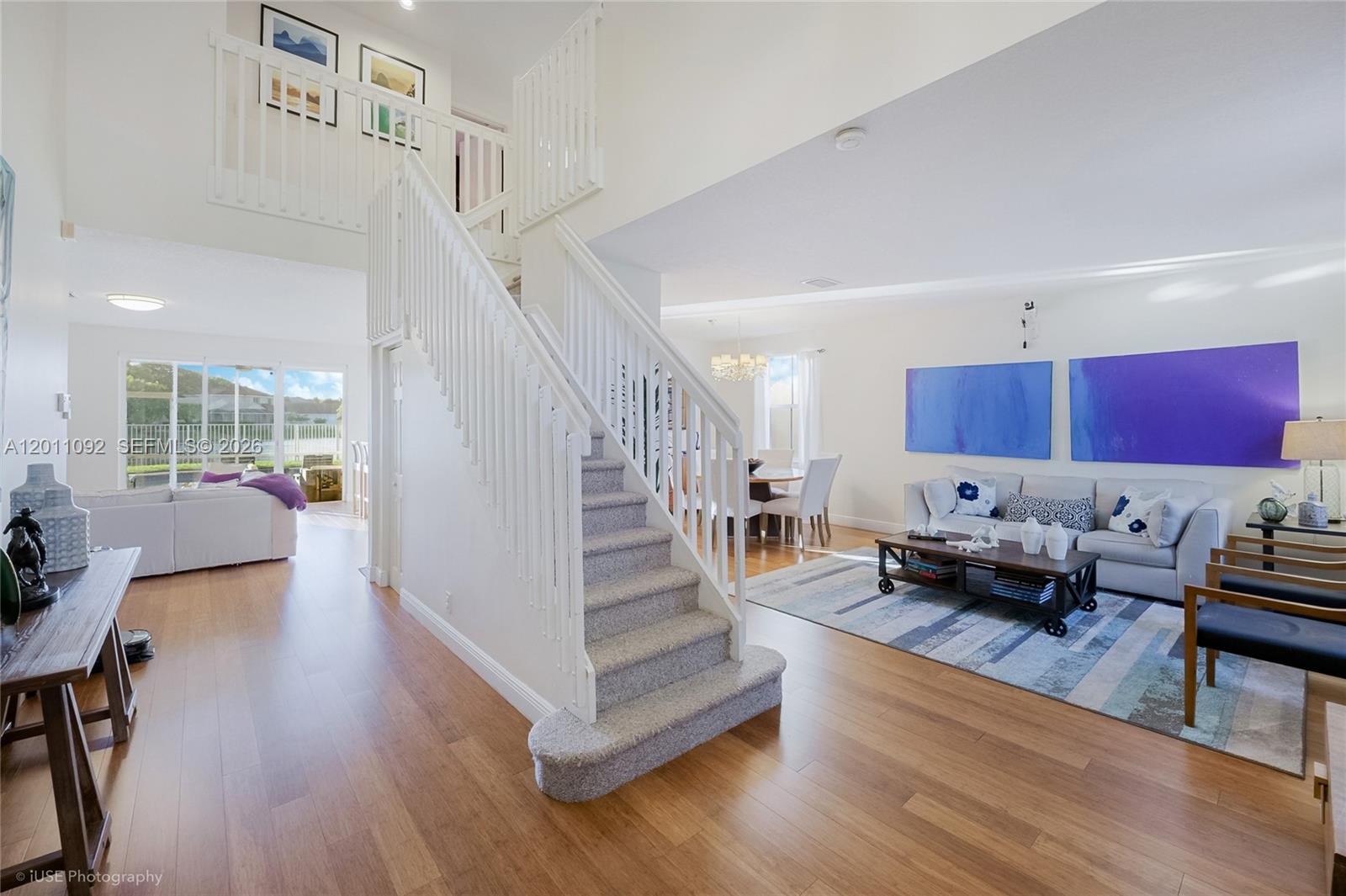 A bright living room features a central staircase, hardwood floors, and blue wall art — 4394 Fox Ridge Dr, Weston FL 33331, WESTON, FL