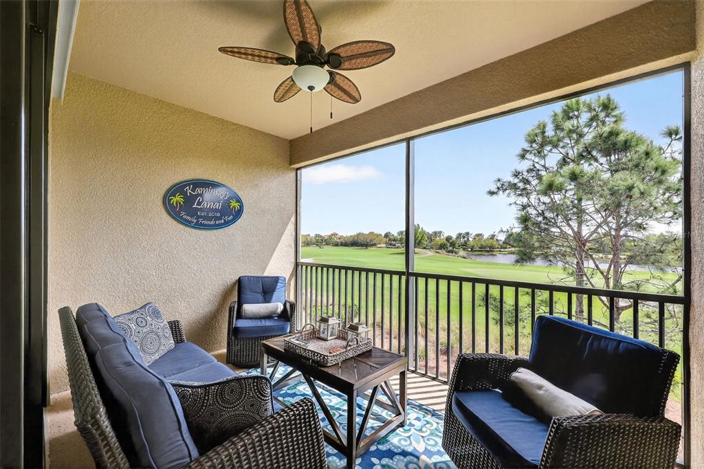 A screened-in balcony features wicker furniture, a ceiling fan, and a view of a golf course — 12660 SORRENTO WAY UNIT 204, BRADENTON, FL